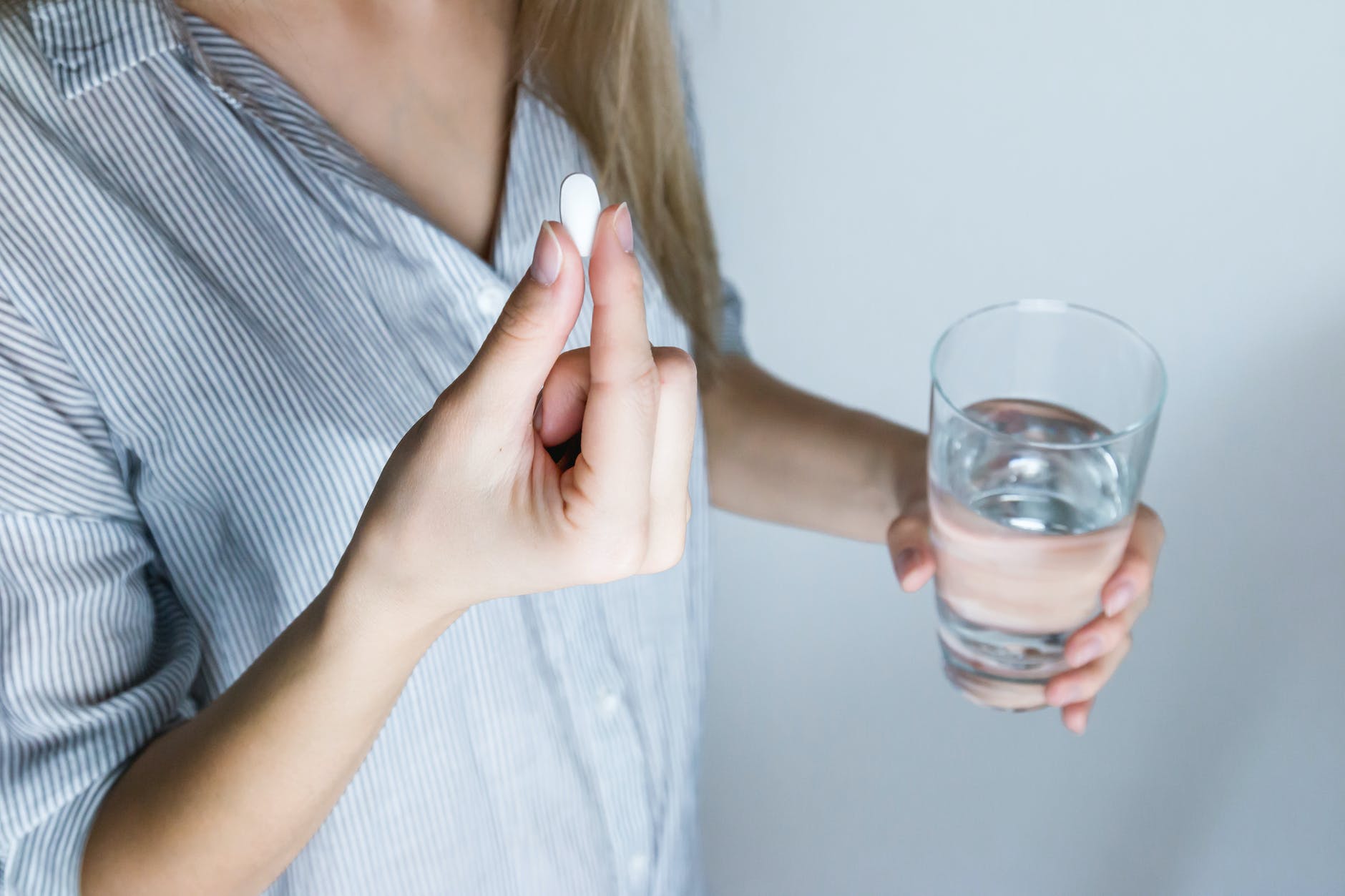 woman holding half full glass and white medicine pill